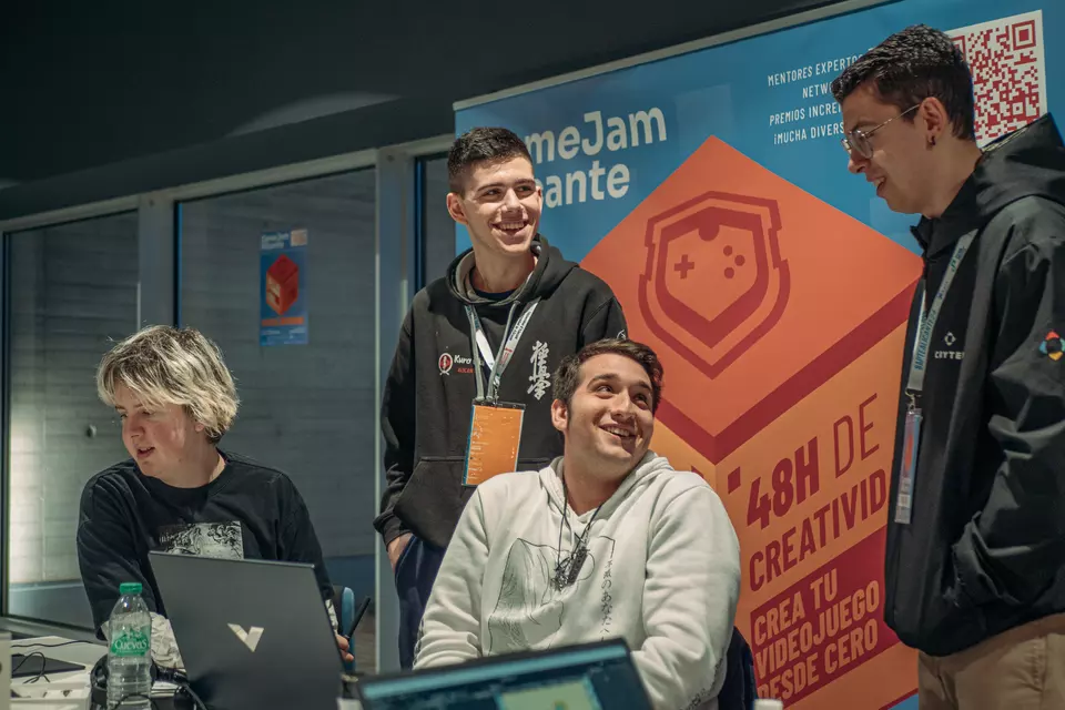 Participantes de la Gamejam Alicante 2025 junto al cartel naranja del evento