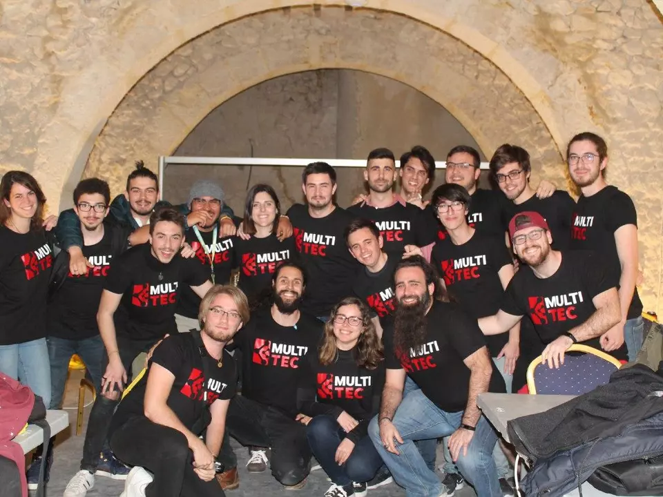 Gran grupo de socios de Multitec con la camiseta de la asociación bajo un arco de piedra